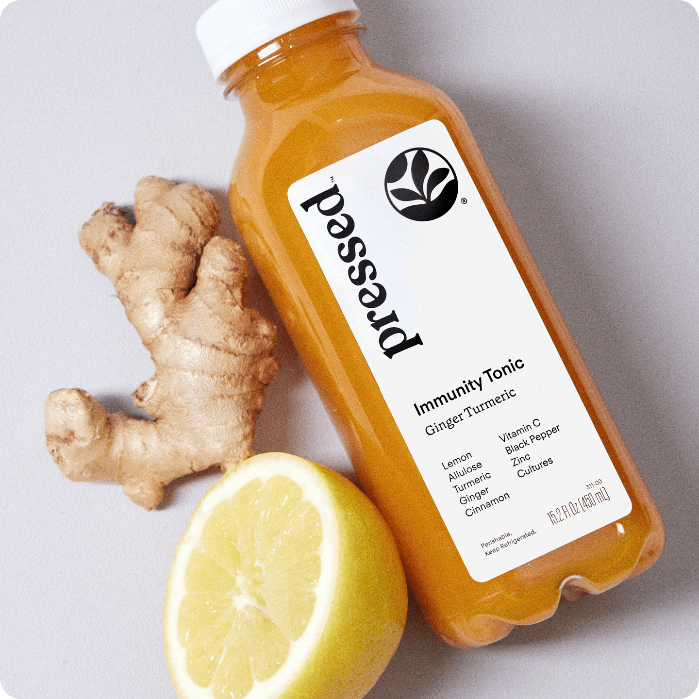 A bottle of Immunity Tonic next to a piece of ginger and half a lemon.