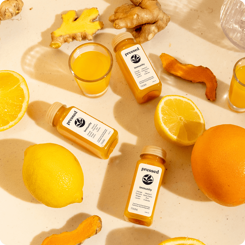 Three immunity shots surrounded by ginger, lemons, and oranges.