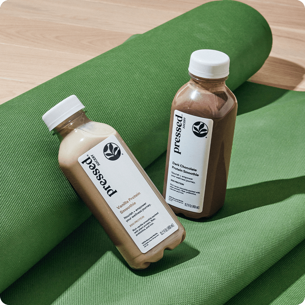 Two bottles of Pressed Juicery smoothies on a green yoga mat.